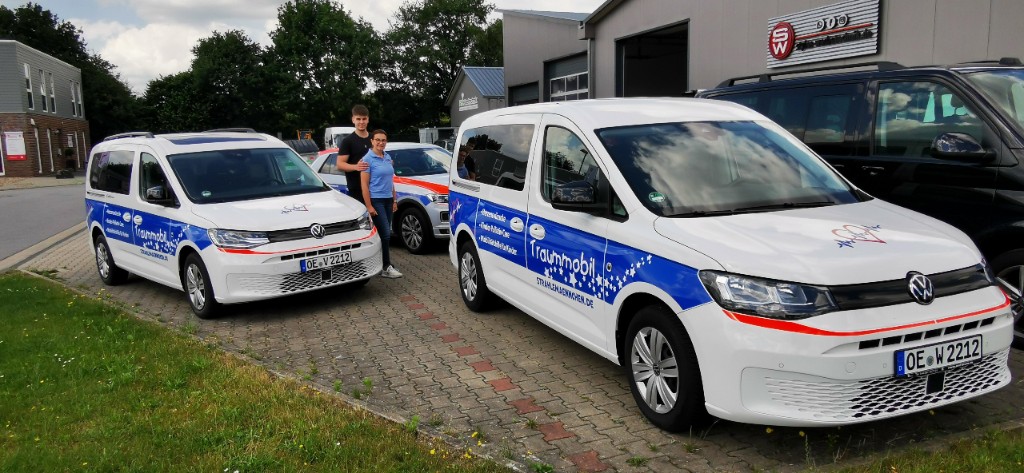 Zwei rollstuhlgerechte Fahrzeuge nebeneinander mit dem Team