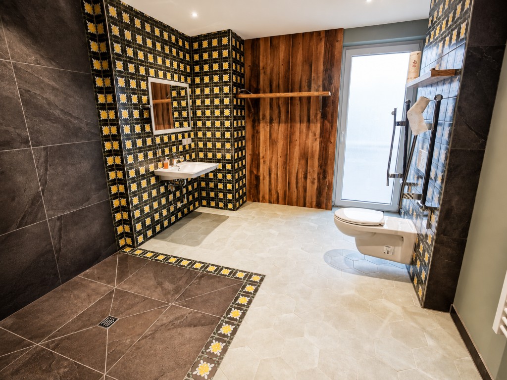 Barrierefreies Badezimmer in Haus Konrad mit schwellenloser bodengleicher Dusche, unterfahrbarem Waschbecken, wandhängendem WC mit Stützgriffen und großer freier Bewegungsfläche