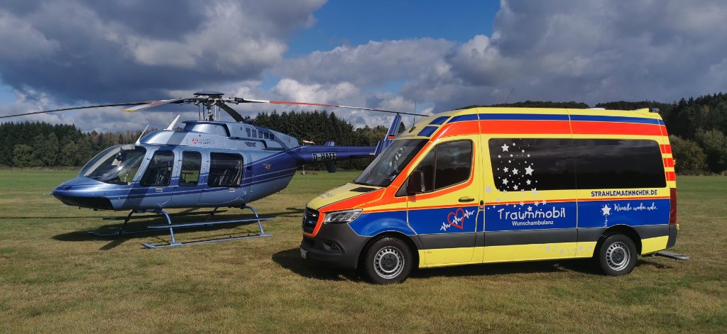 Traummobil-Wunschambulanz neben einem Hubschrauber auf einer Wiese